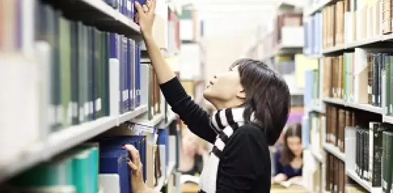 Person looking for a book on a library bookshelf